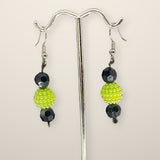 Lime Green Earrings with lime textured berry beads and faceted black beads on silver hooks, shown on a silver stand